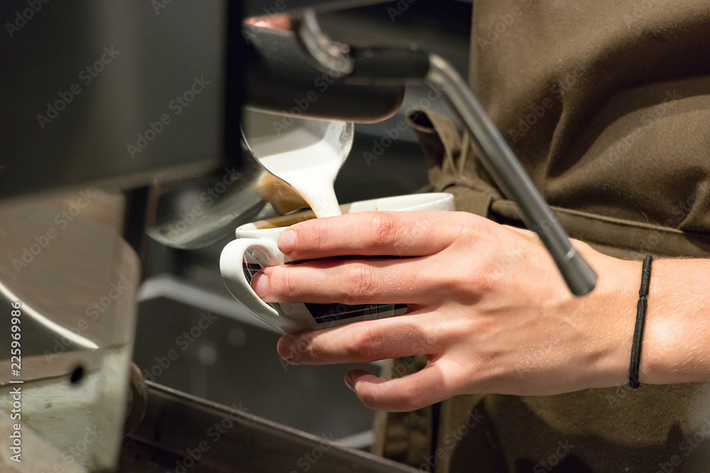 Female barista hands pouring hot milk on a cup to make a cappuccino.