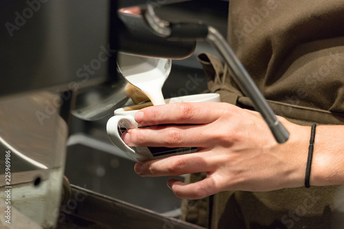 Female barista hands pouring hot milk on a cup to make a cappuccino.