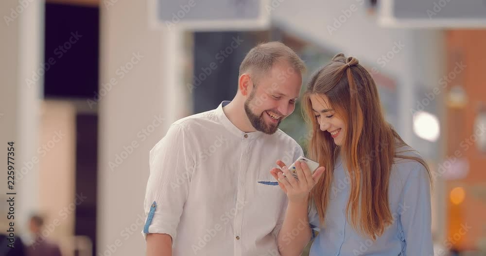 Man and a woman are standing in the mall, looking at the phone, talking and laughing Man and a woman are standing in the mall, looking at the phone, talking and laughing