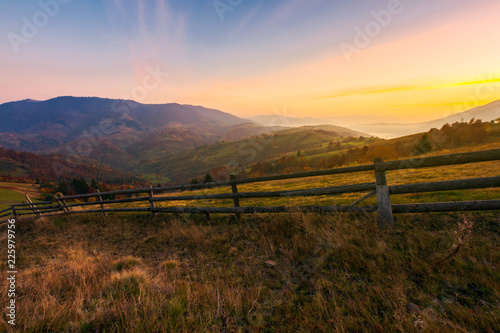 beautiful sunrise in mountains. wonderful countryside scenery in autumn. fence along the rural fields. fog in the distant valley