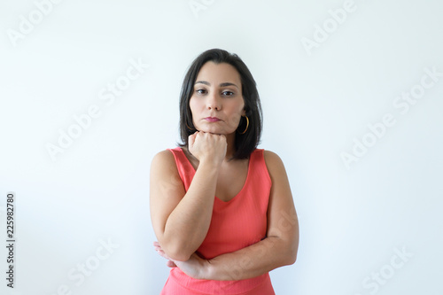Pensive attractive Caucasian woman with pressed lips holding chin. Pretty middle aged woman in pink dress thinking about new solving problem. Business difficulties concept.