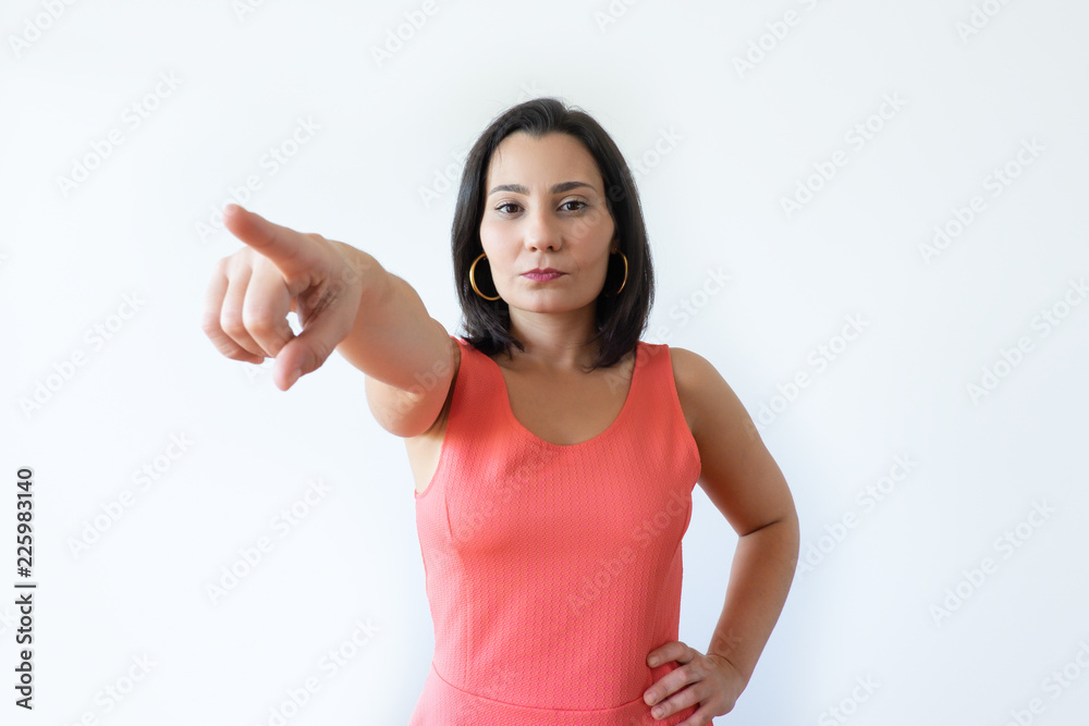 Serious pretty Caucasian woman pointing ahead with index finger. Attractive middle aged woman with pressed lips commanding turning back. Showing door concept. Serious pretty Caucasian woman pointing ahead with index finger. Attractive middle aged woman with pressed lips commanding turning back. Showing door concept.