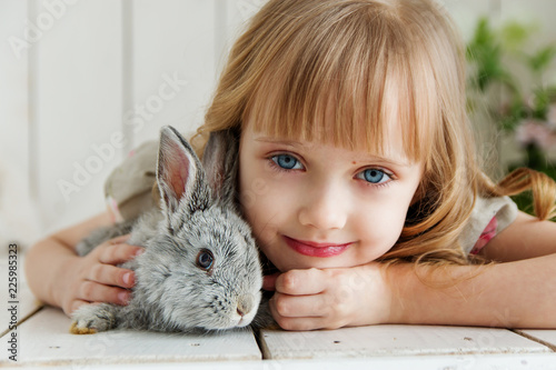 Cute girl hugging with rabbit while lying on the floor at home