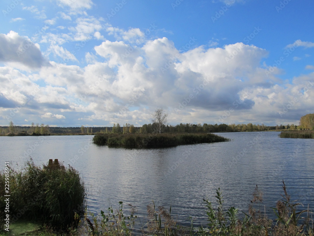 a small island in the middle of the lake with a Sunny day with a bright blue sky and voluminous large clouds