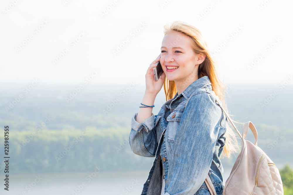 Young happy student girl talking on smartphone and smiling on nature