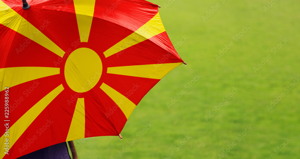 Macedonia flag umbrella. Close up of printed umbrella over green grass lawn / field. Rainy weather forecast concept.	