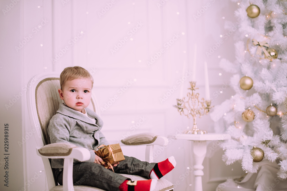 Cheerful little baby boy playing with gifts and presents near Christmas tree, gold and beige pastel c Cheerful little baby boy playing with gifts and presents near Christmas tree, gold and beige pastel c