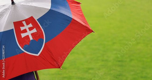 Slovakia flag umbrella. Close up of printed umbrella over green grass lawn / field. Rainy weather forecast concept. 