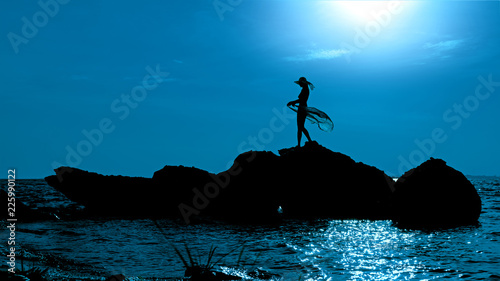 Silhouette of a woman walking along the rocks in the water at night