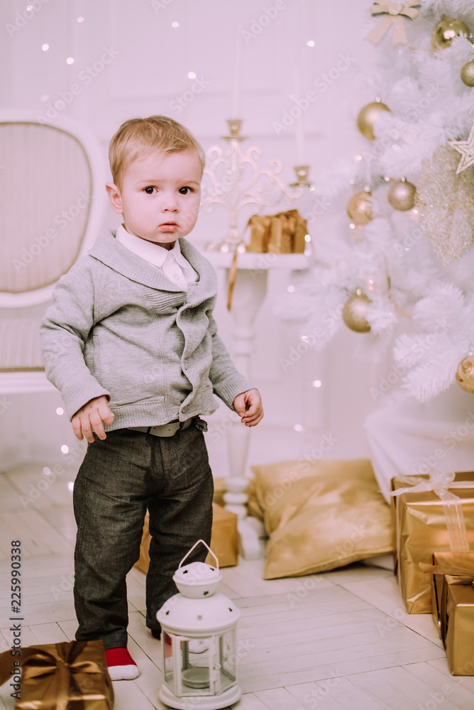 Cheerful little baby boy playing with gifts and presents near Christmas tree, gold and beige pastel c Cheerful little baby boy playing with gifts and presents near Christmas tree, gold and beige pastel c