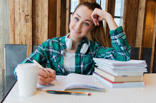 Young beautiful student girl is doing her homework or preparing to the exams siting with books copybooks