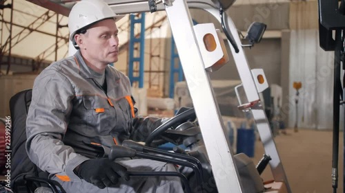 man driving a forklift through a warehouse in a factory. driver in uniform and protective helmet. the concept of logistics and storage