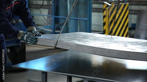 The crane manipulates metal sheets. Workers by means of the crane move a pile of metal sheets in the shop. The faces of employees aren't visible, in a shot only of a hand, parts of bodies.