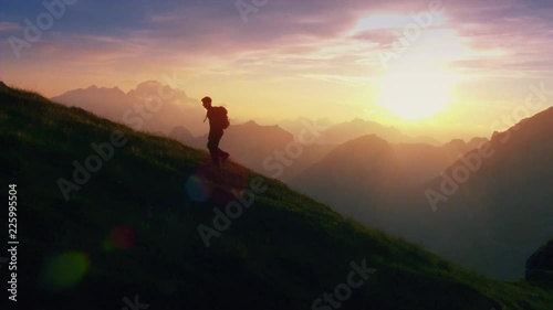 Aerial - Epic shot of a man hiking on the edge of the mountain as a silhouette in colorful sunset (edited) photo