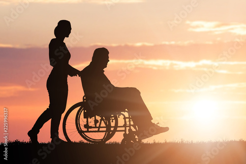 Silhouette Of Woman Assisting Her Disabled Father On Wheelchair