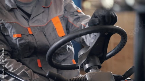close - up steering wheel and levers. man driving a forklift through a warehouse in a factory. driver in uniform and protective helmet. the concept of logistics and storage