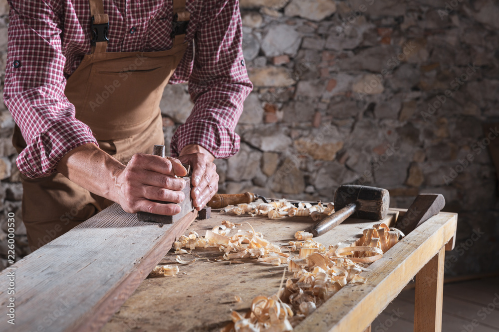 Man scraping plank while it sits on workbench Man scraping plank while it sits on workbench