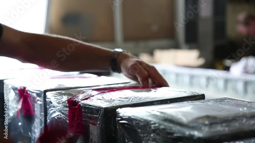 Gluing of a tape on packing. Red film. Safes are packed in a film. Warehouse. Natural lighting. Gluing device. Work is carried out by the employee. Close up.
