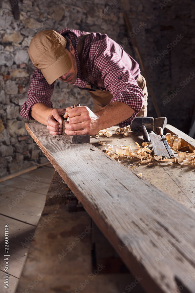Carpenter smoothing out long wooden beam with tool Carpenter smoothing out long wooden beam with tool