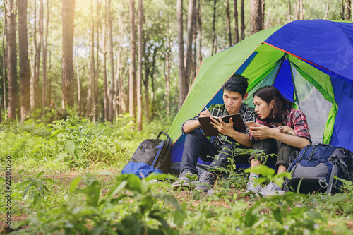 Asian couples using smartphone and make a short note in the tent. Camping trip in nature.