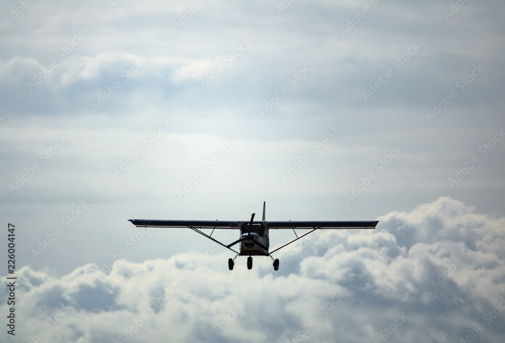 Light aircraft flying over cloudy sky, front view