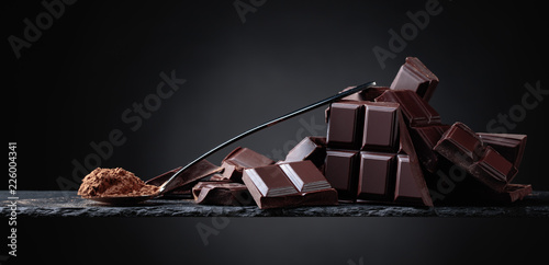 Broken chocolate pieces and cocoa powder on black background.
