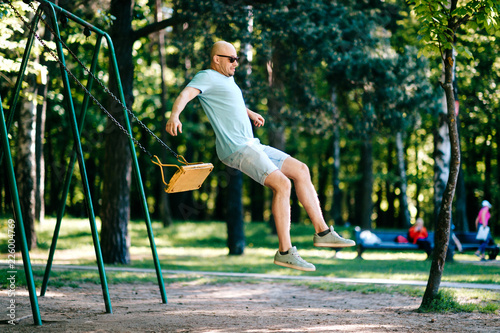 Tableau sur toile Odd adult bald man in sunglasses jumping from swing on ground in motion