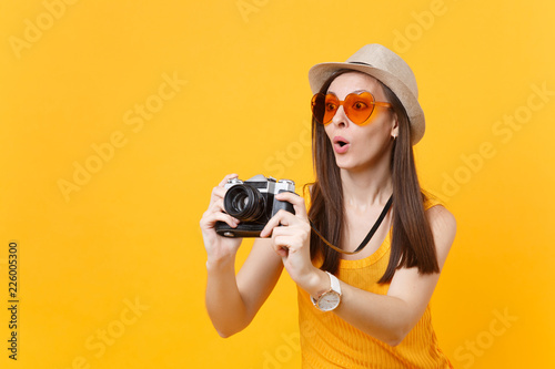 Tourist woman in summer casual clothes, hat take picture on retro vintage photo camera isolated on yellow background. Girl traveling abroad to travel on weekends getaway. Air flight journey concept.