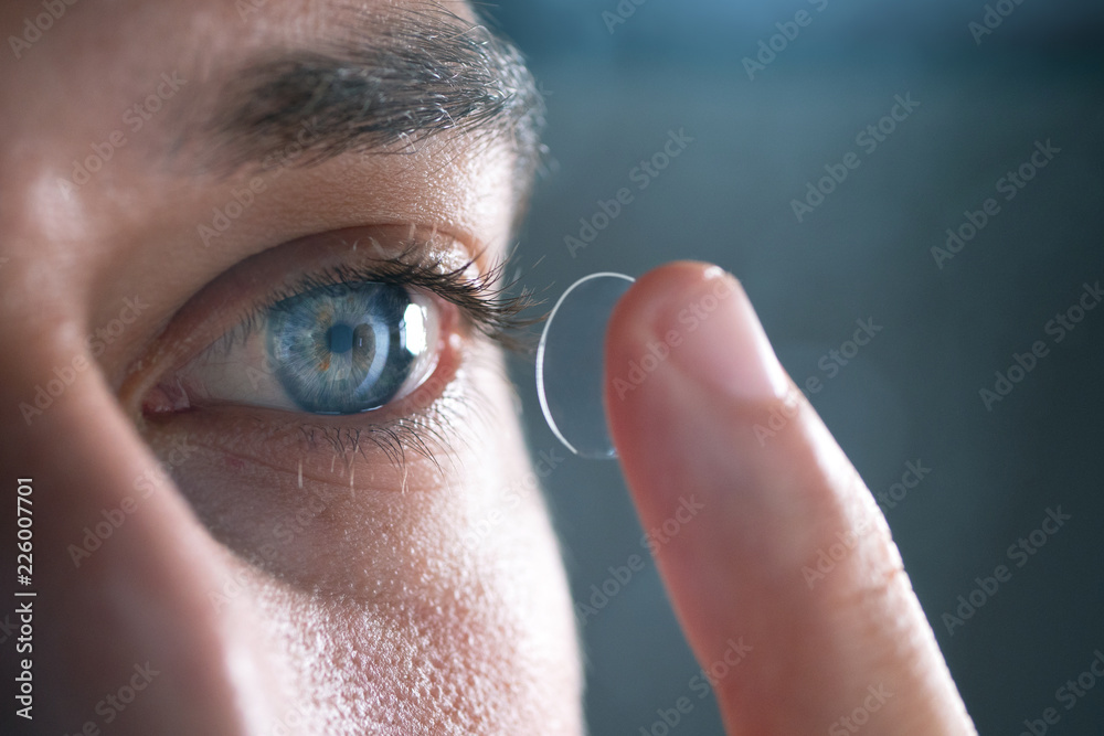 Close-up of a man putting contact lenses on blue eye. Concept of: healtcare, optic, hydration of the eye. - obrazy, fototapety, plakaty 