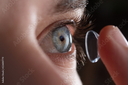 Close-up of a man putting contact lenses on blue eye. Concept of: healtcare, optic, hydration of the eye. photo