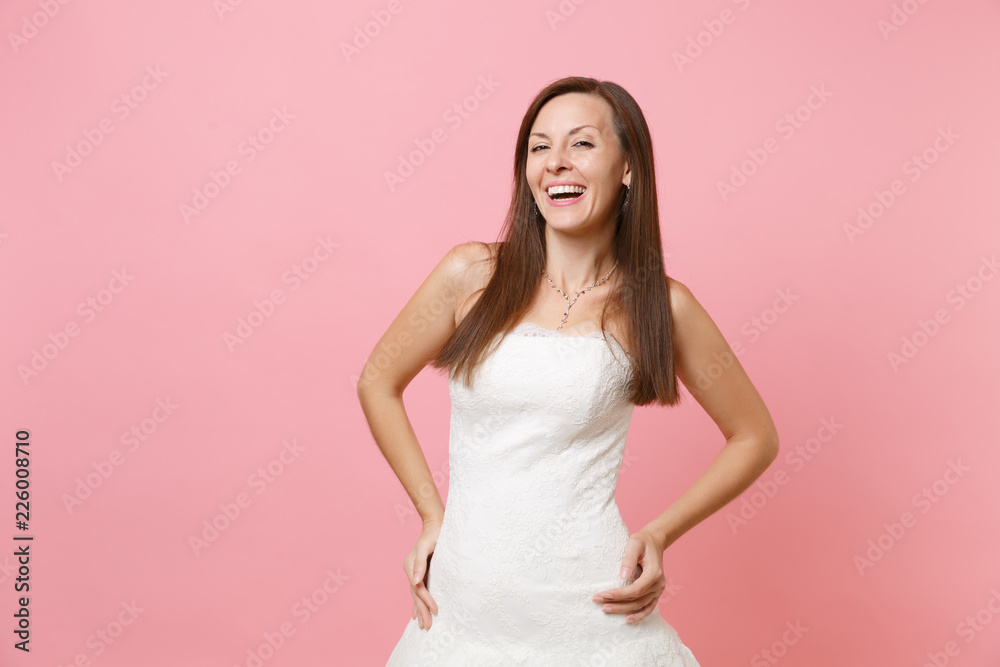 Portrait of laughing happy bride woman in elegant white wedding lace dress standing with arms akimbo isolated on pink pastel background. Wedding celebration concept. Copy space for advertisement. Portrait of laughing happy bride woman in elegant white wedding lace dress standing with arms akimbo isolated on pink pastel background. Wedding celebration concept. Copy space for advertisement.