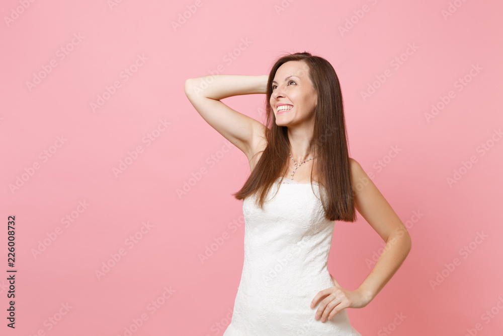 Portrait of joyful dreamy bride woman in elegant white wedding dress standing and keeping hand near head isolated on pink pastel background. Wedding celebration concept. Copy space for advertisement. Portrait of joyful dreamy bride woman in elegant white wedding dress standing and keeping hand near head isolated on pink pastel background. Wedding celebration concept. Copy space for advertisement.