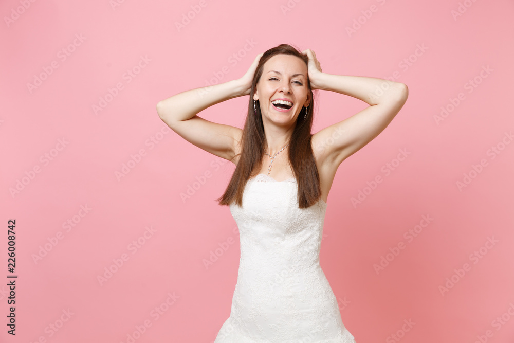 Portrait of happy cheerful bride woman in beautiful white wedding dress standing keeping hands near head isolated on pink pastel background. Wedding celebration concept. Copy space for advertisement. Portrait of happy cheerful bride woman in beautiful white wedding dress standing keeping hands near head isolated on pink pastel background. Wedding celebration concept. Copy space for advertisement.