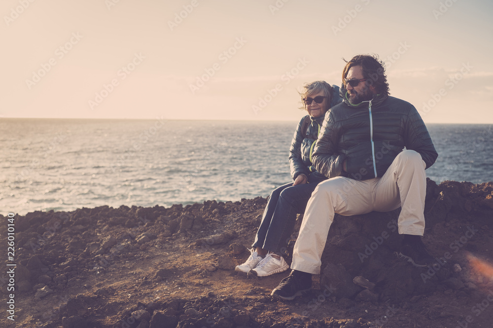 Mother and son spend time together sitting on a rock smiling and looking at sea and mountains. trekking and travel concept for alternative vacation or leisure activity. vintage colors