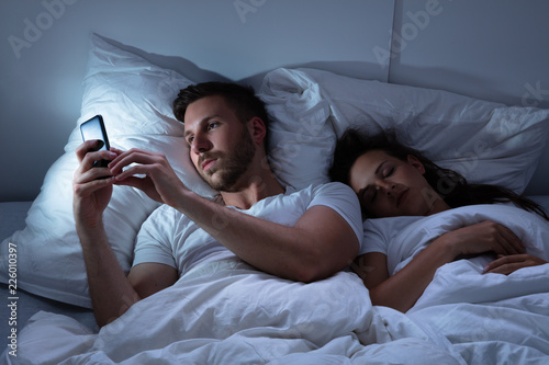 Leinwand Poster Man Using Cellphone While Her Wife Sitting On Bed