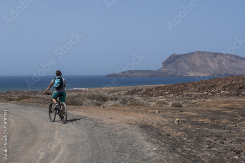 Lanzarote, isole Canarie: ragazzo di spalle in bicicletta sulla strada sterrata per la spiaggia Playa de Las Concisa sull'isola La Graciosa