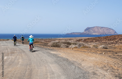 Lanzarote, isole Canarie: turisti di spalle in bicicletta sulla strada sterrata per la spiaggia Playa de Las Concisa sull'isola La Graciosa