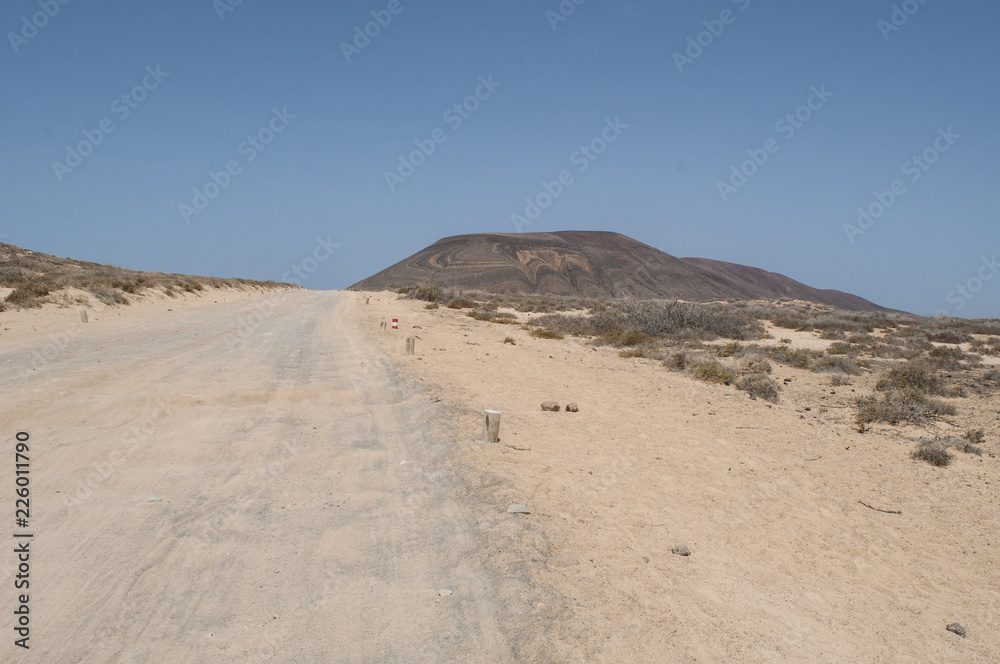 Lanzarote, Isole Canarie: strada sterrata, cespugli e paesaggio desertico con la Montagna Pedro Barba, il vulcano dell'isola La Graciosa