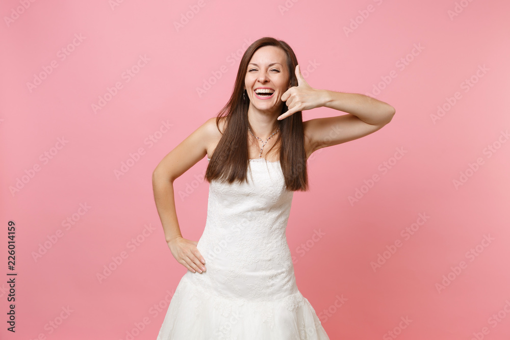 Joyful bride woman in wedding dress doing phone gesture like says: call me back with hand and fingers like talking on telephone isolated on pink background. Communicating. Wedding concept. Copy space. Joyful bride woman in wedding dress doing phone gesture like says: call me back with hand and fingers like talking on telephone isolated on pink background. Communicating. Wedding concept. Copy space.