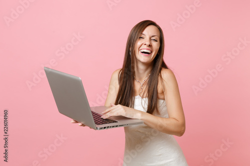 Portrait of laughing happy bride woman in wedding dress planning wedding, working on laptop pc computer isolated on pastel pink background. Wedding to do list. Organization of celebration. Copy space.