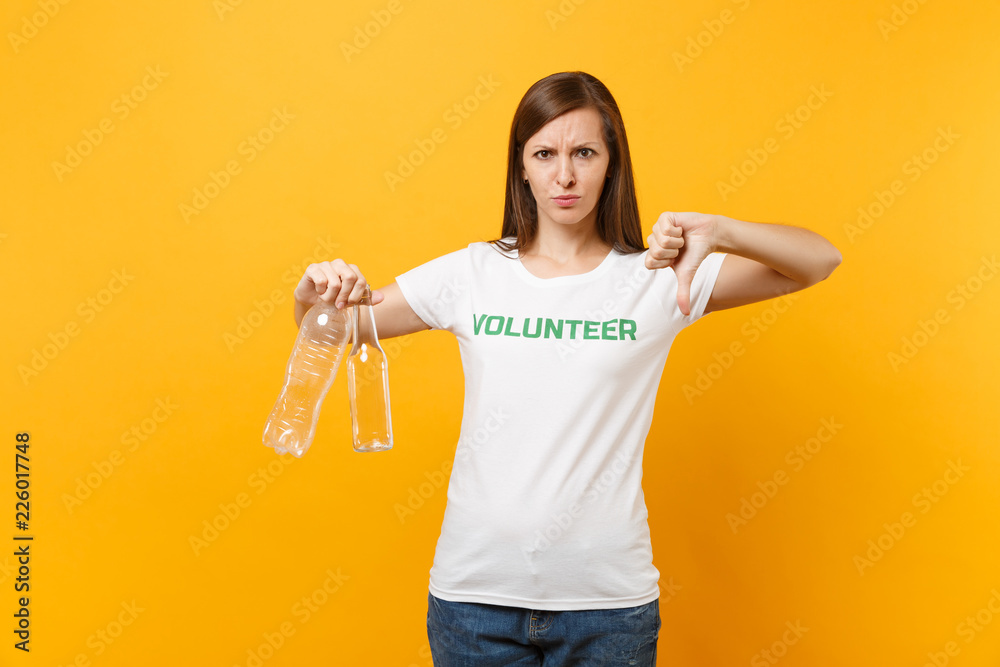 Woman portrait in white t-shirt with written inscription green title volunteer hold plastic and glass bottles isolated on yellow background. Voluntary free assistance help, trash sorting work concept. Woman portrait in white t-shirt with written inscription green title volunteer hold plastic and glass bottles isolated on yellow background. Voluntary free assistance help, trash sorting work concept.