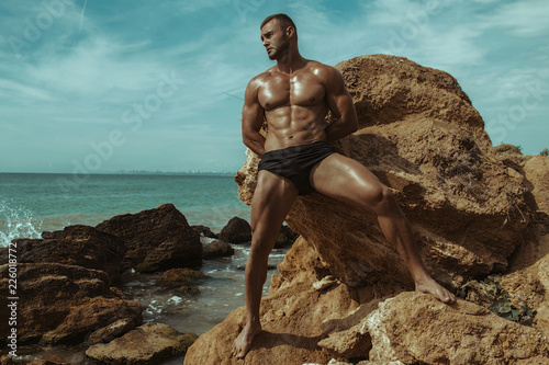 Canvas Print Strong face muscle male model on the nature background with sand stones and wate