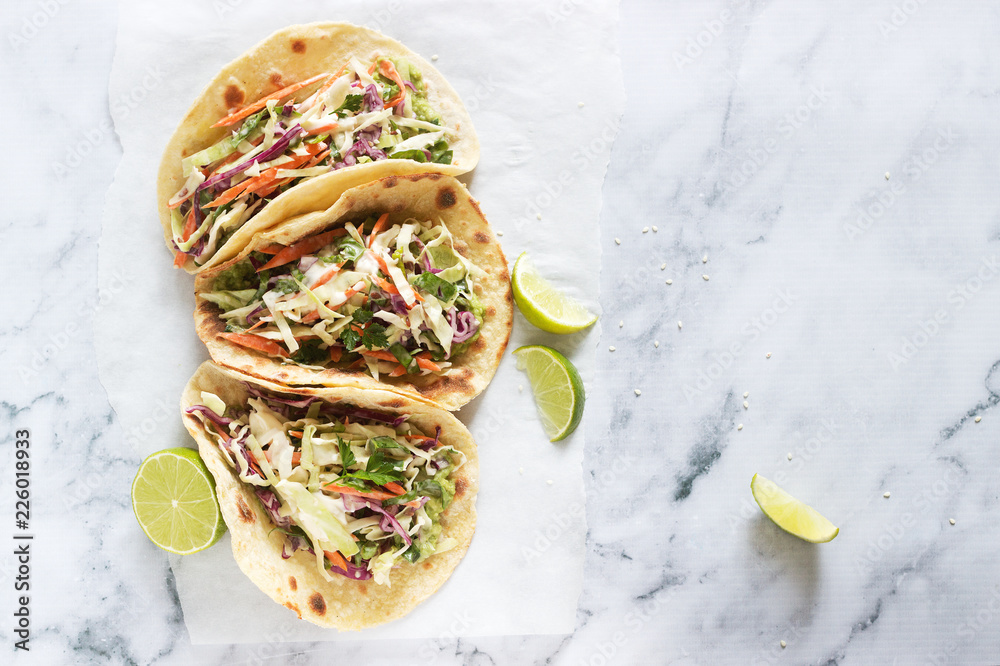 Tacos with guacamole and coleslaw served with lime slices on a light background.