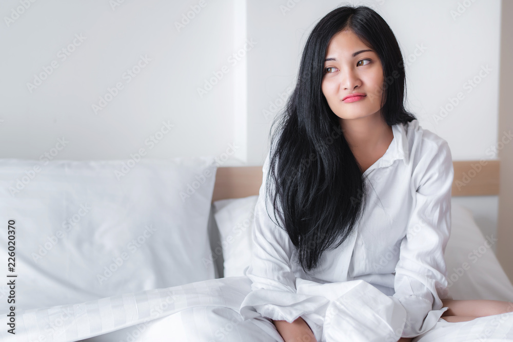 Beautiful young pretty Asian woman wake up and make happy smile with white shirt at the white bed in the morning Beautiful young pretty Asian woman wake up and make happy smile with white shirt at the white bed in the morning