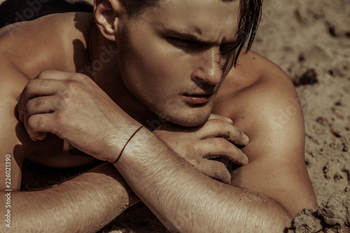 Strong face male model on the nature background with sand and water and sky on the beach on the sunset