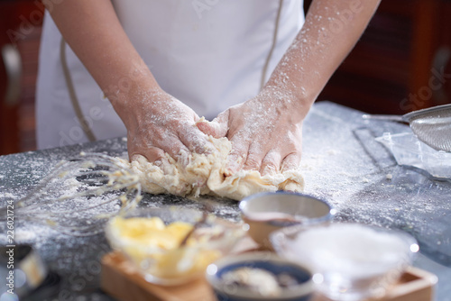 Close-up view of anonymous woman kneading cookie dough on kitchen table covered with flour