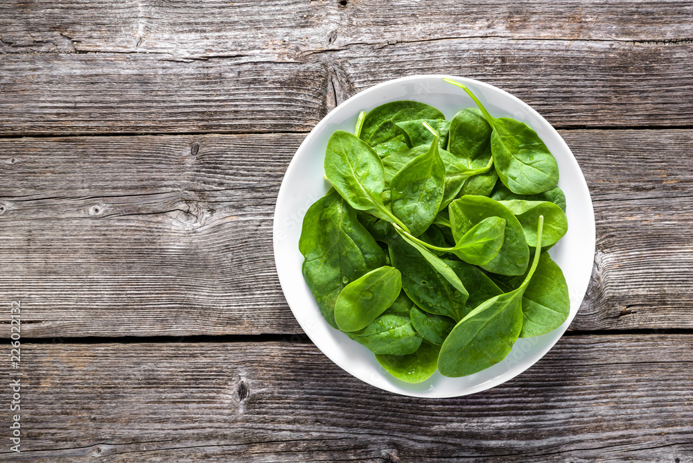 Fresh vegetables, green spinach on plate, top view on wooden table Fresh vegetables, green spinach on plate, top view on wooden table