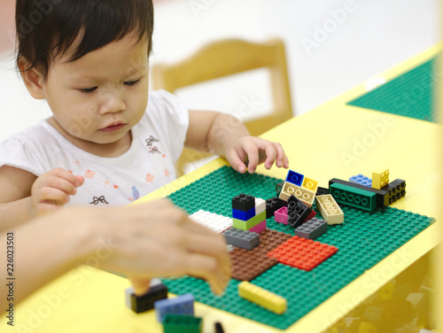 Asian baby playing puzzle toys with parent on yellow table indoor