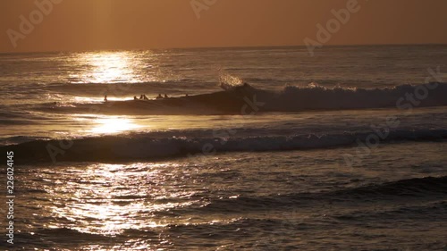 Surfer riding a wave in silhouette against setting sun - SLOMO photo