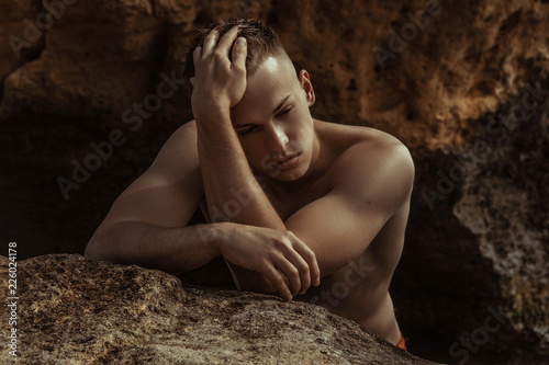 Strong face muscle male model on the nature background with sand stones and water on the beach on the sunset
